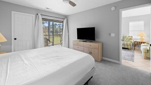 Ein Schlafzimmer mit einem Bett, einem Fernseher auf einer Holzkommode, einem Deckenventilator und Blick auf eine Terrasse mit Sitzgelegenheiten.
