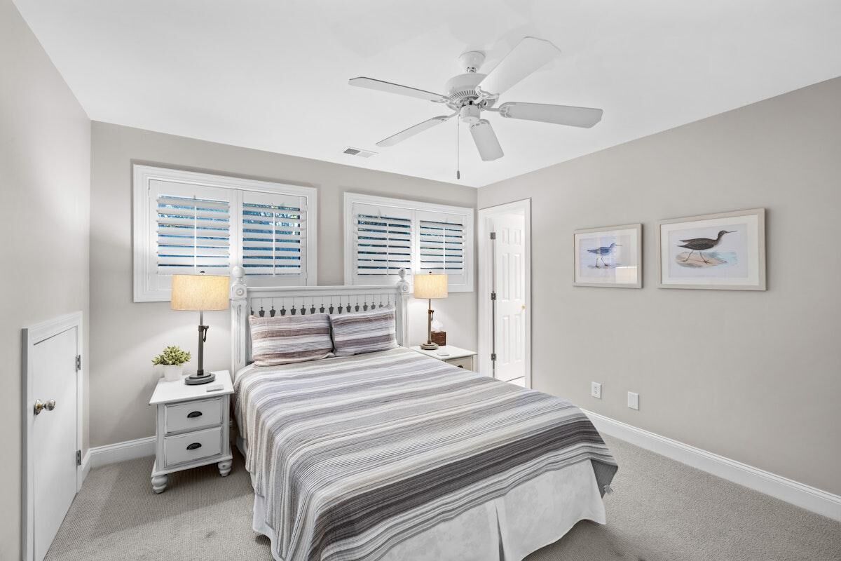 A bedroom with a bed, nightstands, a ceiling fan, and two windows with blinds.