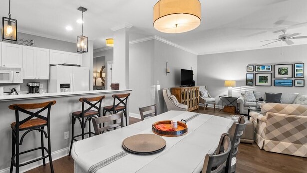 Una cocina moderna con armarios blancos, un comedor con mesa y sillas blancas, y una sala de estar con sofá y televisor.