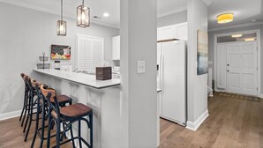 Una cocina moderna con una isla central, taburetes de bar, iluminación colgante y un refrigerador.