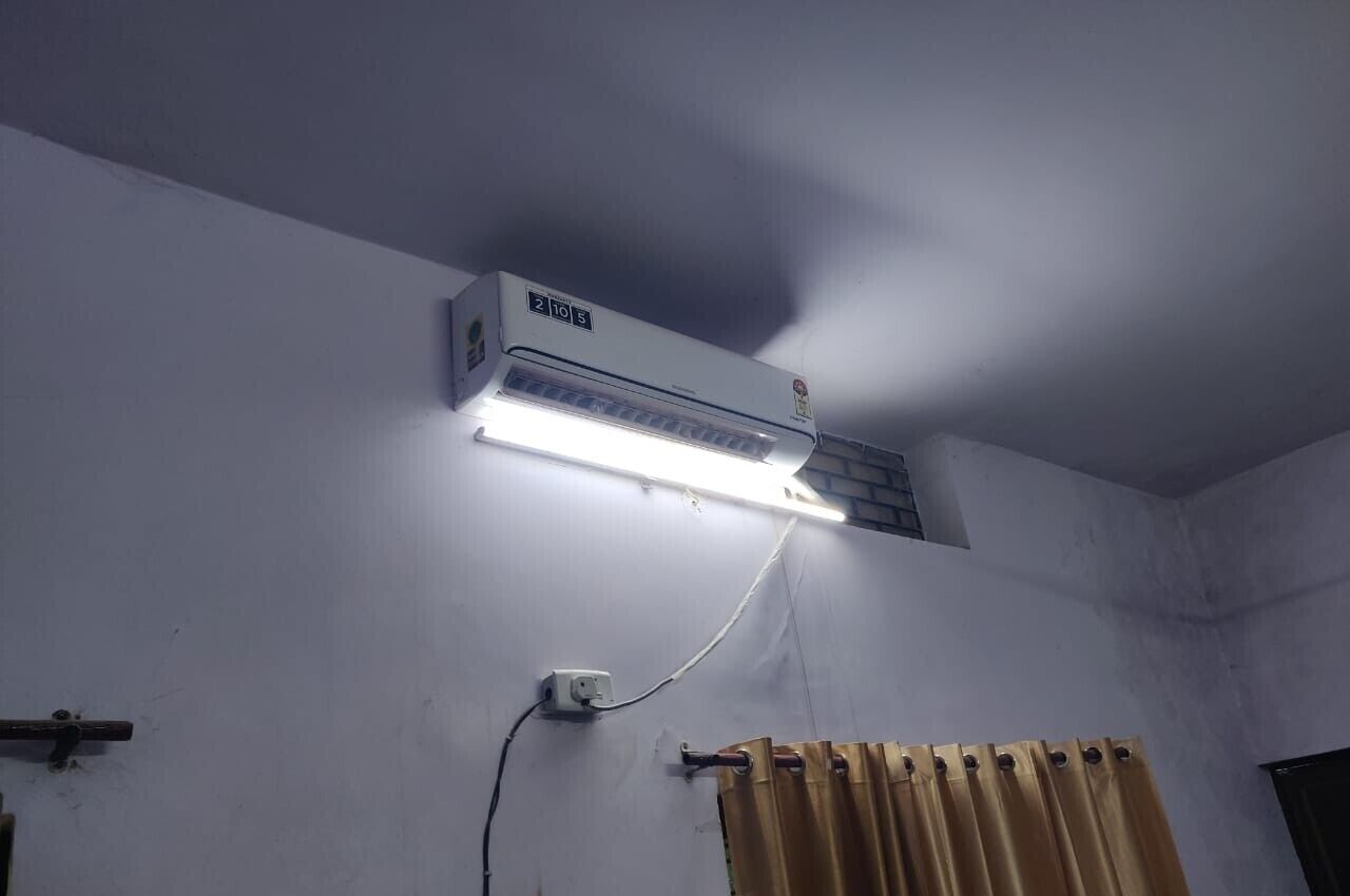 An air conditioning unit mounted on a wall with a visible power outlet and a curtain rod.