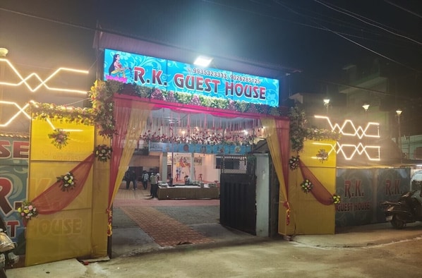 The entrance to R.K. Guest House with a neon sign, decorated with flowers and drapes.