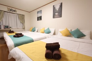 A hotel room with two beds, each with white bedding and yellow and teal pillows. There are rolled towels on the beds and a 'Welcome' sign on the wall. - Convenient Nakano House Near the Train Station - Ideal for Budget Travelers (21) (中野区中央)