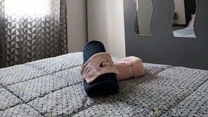 Un dormitorio con una colcha estampada, un espejo grande con marco ondulado y una ventana con cortinas geométricas.