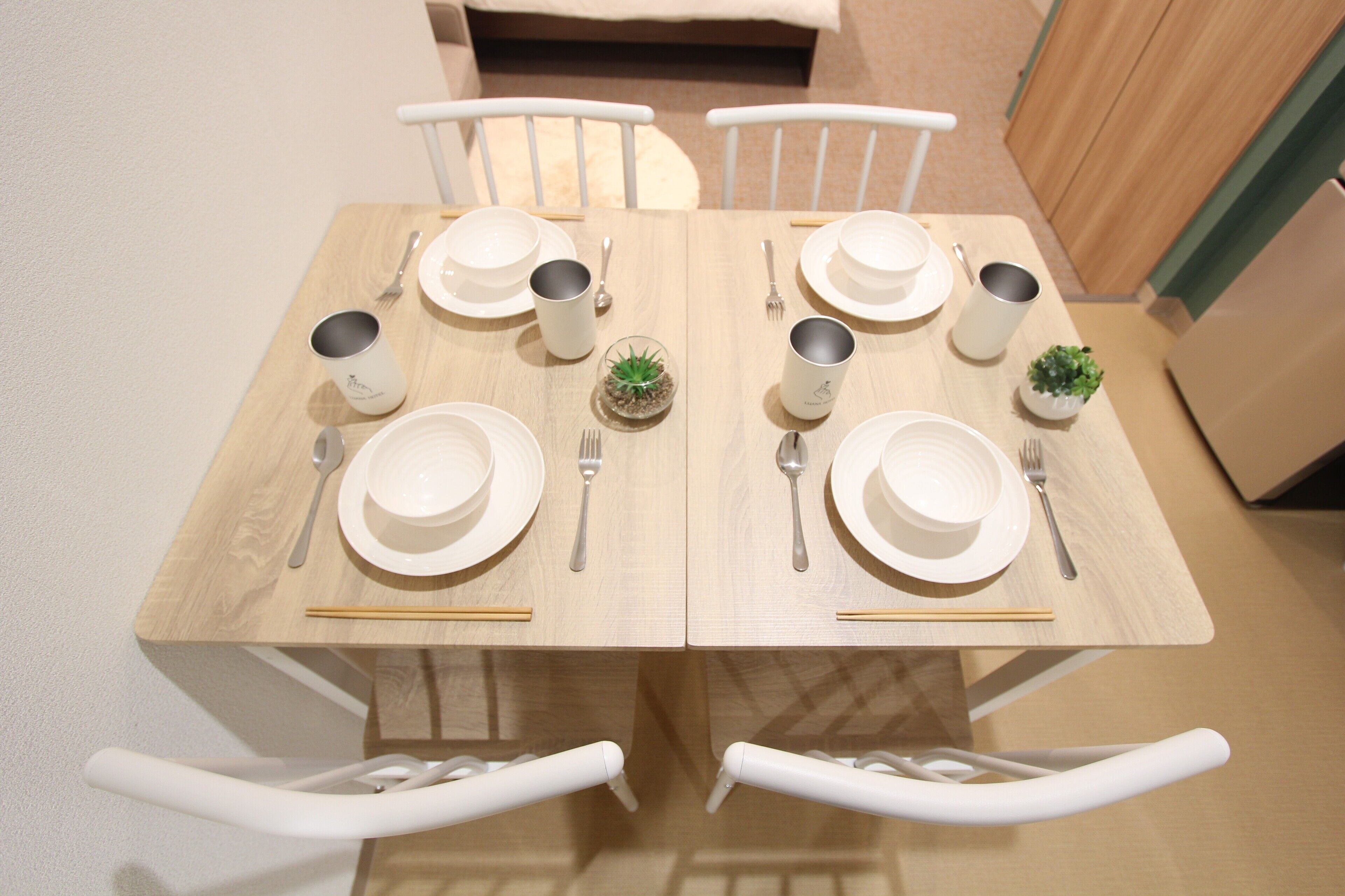A dining table set with white plates, bowls, and cups, accompanied by chopsticks and cutlery.