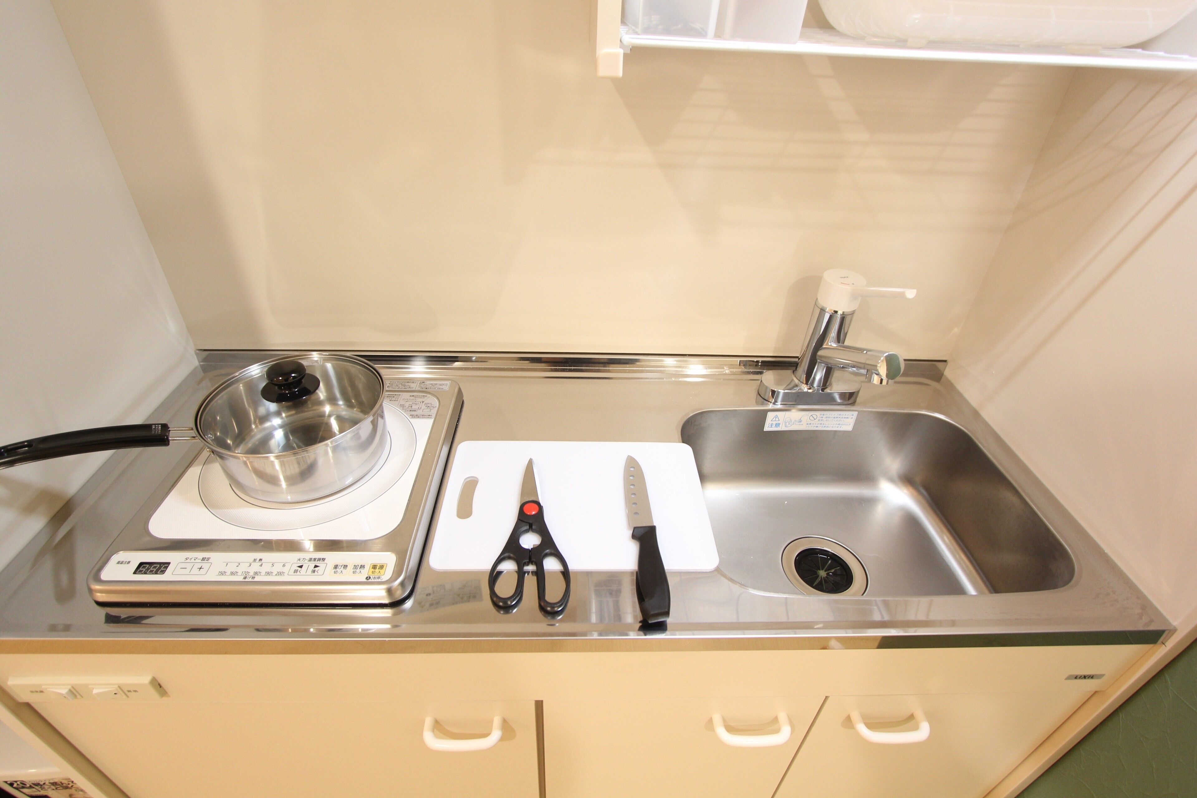 A kitchen with a stove, a sink, and a countertop with a pot, a pair of scissors, and a knife.