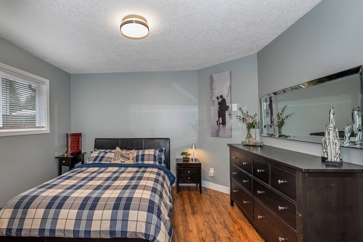 A bedroom with a bed, dresser, nightstand, and a large mirror.