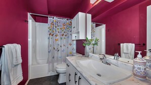 A bathroom with a white sink, a toilet, a shower with a butterfly curtain, and a vase with flowers on the counter. - Knockan Hill Rentals-Ground Floor Suite (Victoria)