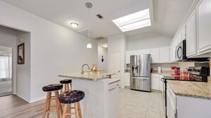 Una cocina moderna con armarios blancos, electrodomésticos de acero inoxidable y una isla central con taburetes.