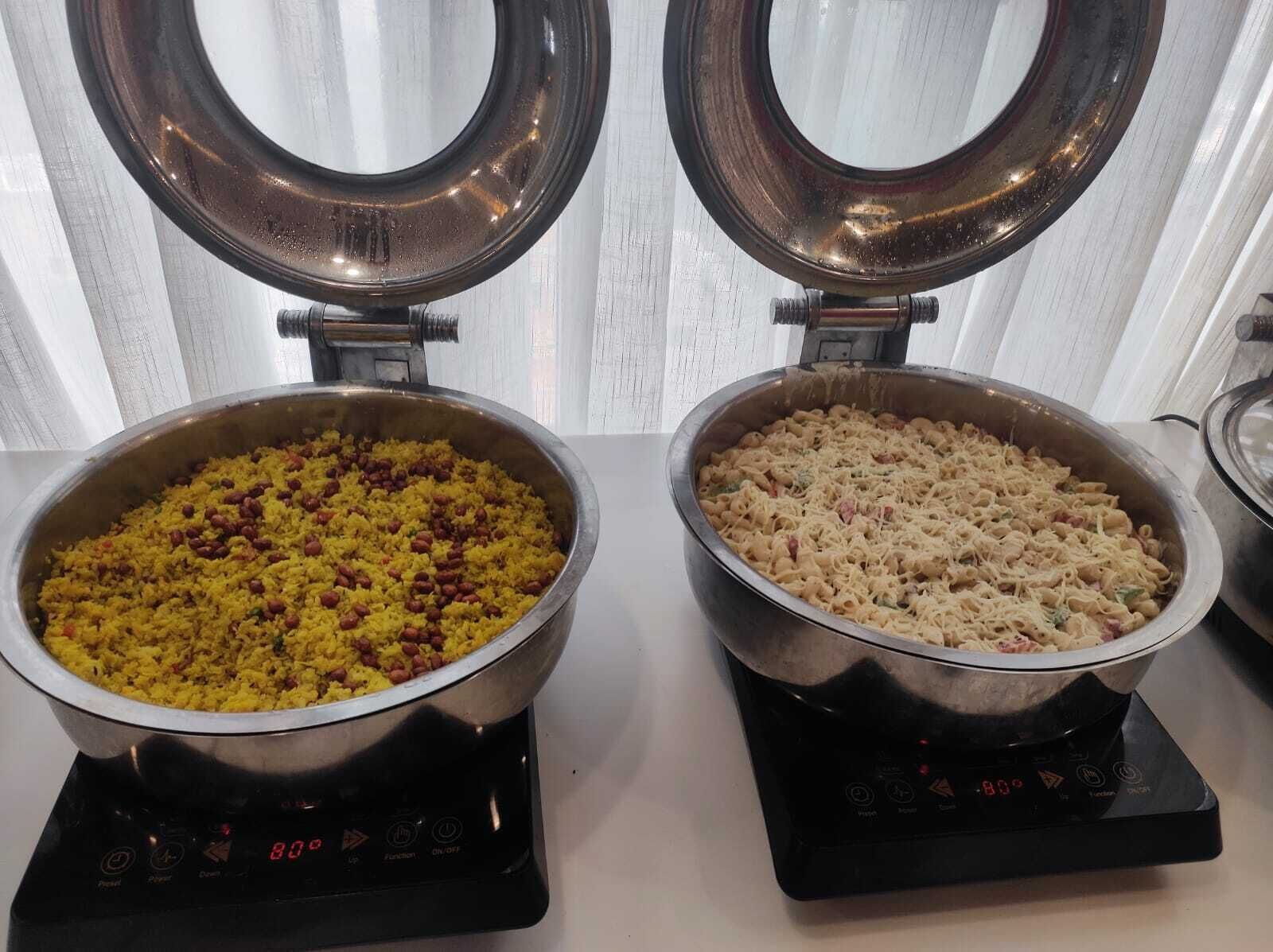 Dos ollas de acero inoxidable sobre cocinas por inducción, una con arroz amarillo y frijoles, y la otra con pasta y queso.