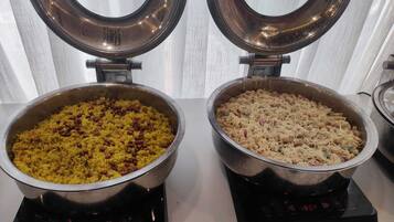 Dos ollas de acero inoxidable sobre cocinas por inducción, una con arroz amarillo y frijoles, y la otra con pasta y queso.