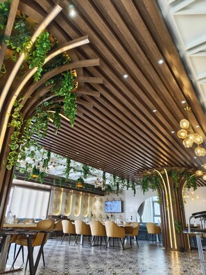 Un restaurant moderne avec un décor intérieur comprenant un plafond en bois, des plantes vertes et un coin bar équipé d’un téléviseur.