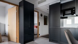 A modern kitchen with built-in appliances, a dining area with a chair, and a bedroom with a bed and a red pillow. - Le Chalet Lingonberry D6 by Aavalevi (Levi)