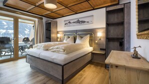 A modern bedroom with a large bed, wooden ceiling, and a mountain view through the glass door.
