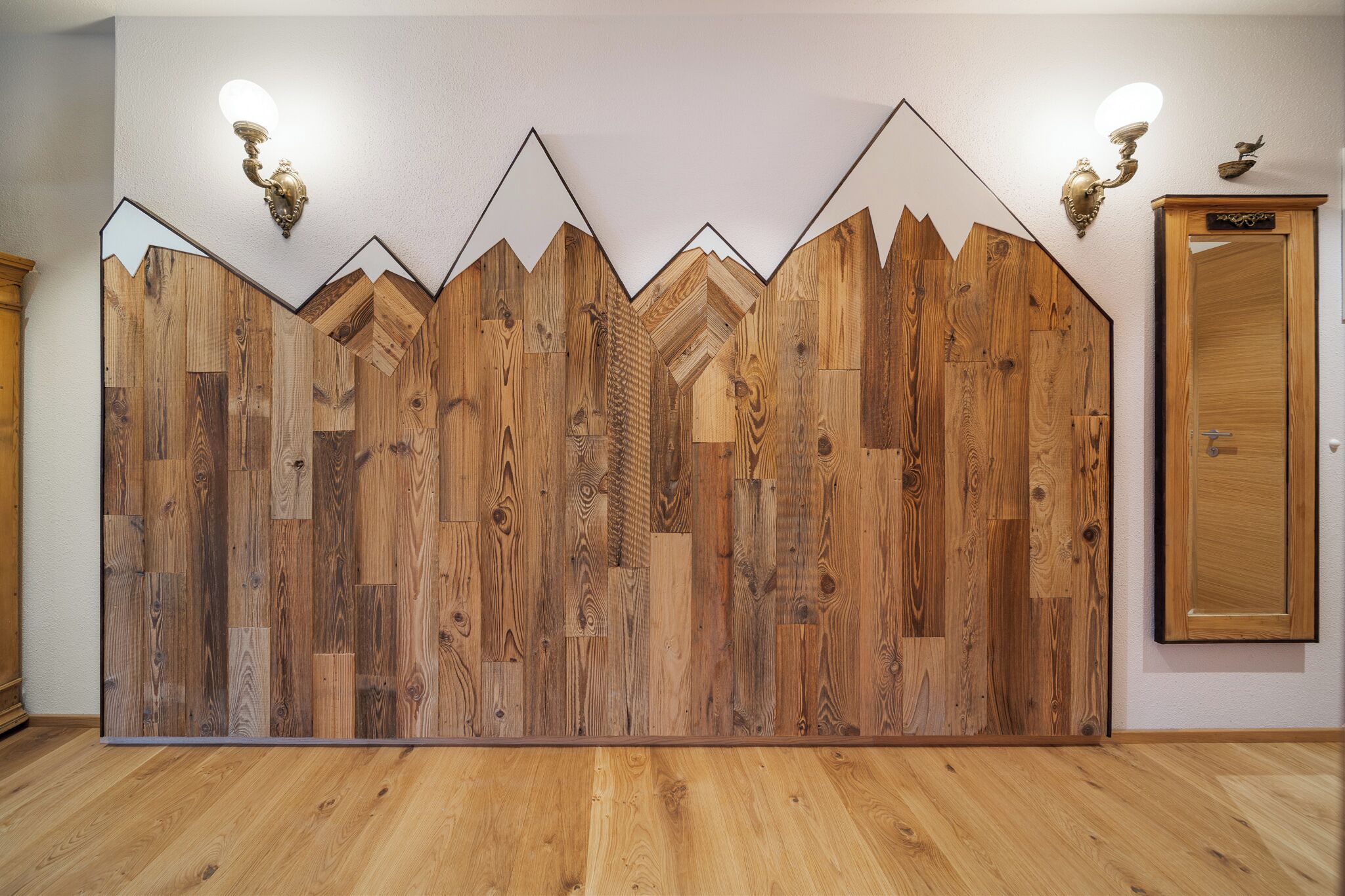 Une pièce dont un mur est recouvert de panneaux en bois, avec une porte en bois et deux appliques murales.