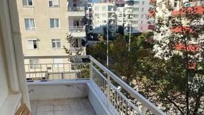 A balcony with a wooden table and chairs, a white railing, and a view of surrounding buildings and trees. - SOYDAN WORLD TRAVEL APART HOTEL (Antalya)