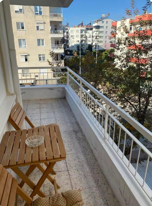 A balcony with a wooden table and chairs, a white railing, and a view of surrounding buildings and trees. - SOYDAN WORLD TRAVEL APART HOTEL (Antalya)