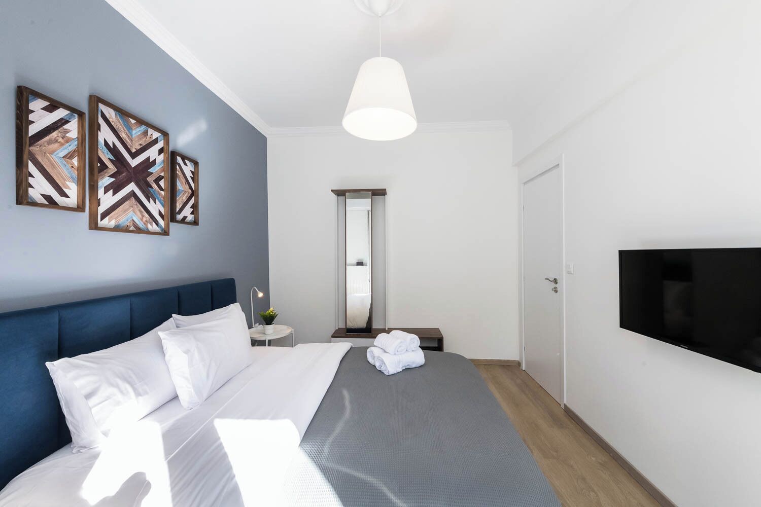 Ett modernt hotellrum med en stor säng, en platt-TV och tre abstrakta konstverk på väggen.