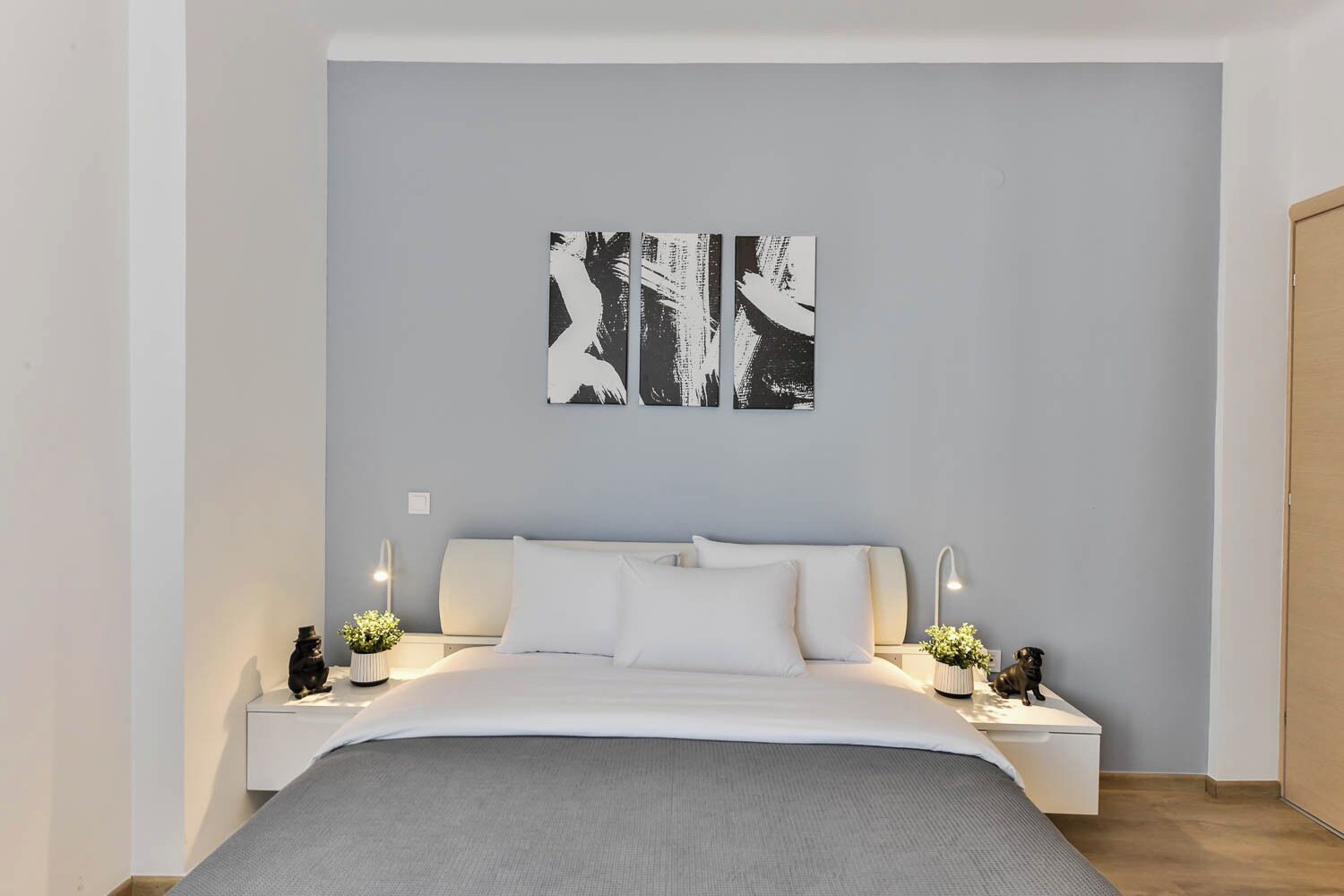 A modern bedroom with a large bed, two bedside tables with lamps, and abstract wall art.