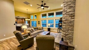 A spacious living room with a sofa, armchairs, and a coffee table. A kitchen is visible in the background, and there is a stone accent wall. - Modern Mountain Family Home on Ski Hill Road — Pet Friendly + A/C (Driggs)