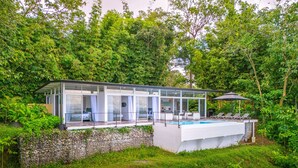 Une maison moderne dotée d’un patio entièrement vitré, d’une piscine et d’une végétation luxuriante qui l’entoure.
