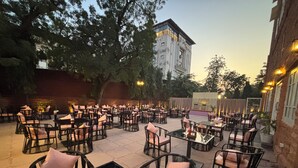 An outdoor seating area with tables and chairs, surrounded by trees and a building in the background. - Surya Niwas Boutique Hotel & Garden (Jodhpur)