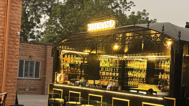 An outdoor bar with a neon sign, multiple shelves of bottles, and several chairs. - Surya Niwas Boutique Hotel & Garden (Jodhpur)
