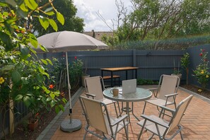 Une terrasse avec une table ronde, quatre chaises, un ordinateur portable et un grand parasol.