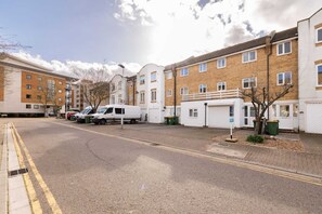 Une rue résidentielle bordée de maisons, avec des véhicules garés et un ciel dégagé.