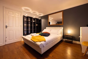 Une chambre avec un lit blanc, un grand miroir, un plancher en bois et une bibliothèque intégrée.