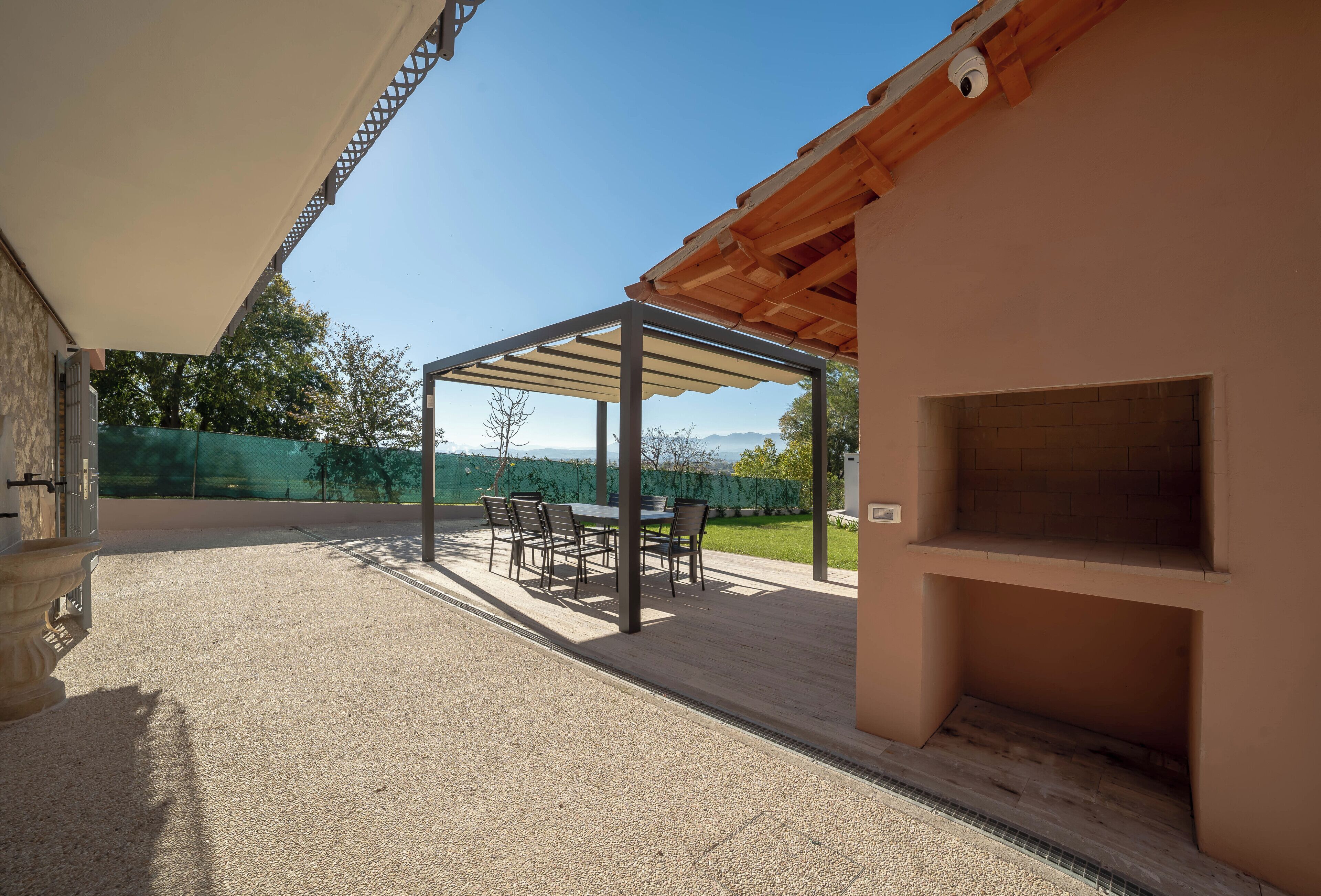An outdoor patio with a covered seating area, a barbecue grill, and a stone planter.