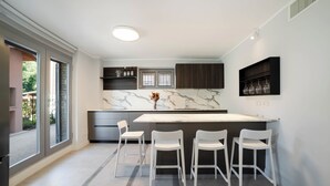 Una cocina moderna con encimera de mármol, sillas blancas y una estantería empotrada para vinos.
