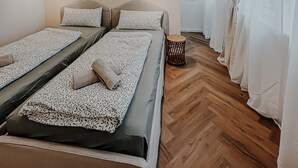 Una camera d'albergo moderna con due letti singoli, un'ampia finestra con tende leggere e un pavimento in legno, illuminata da un lampadario a soffitto.