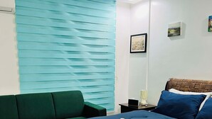 A bedroom with a bed, green sofa, and a window with blue blinds. - Cozy 1 bedroom condo inside Subic Bay Freeport Zone with complete amenities. (Subic Bay Freeport Zone)