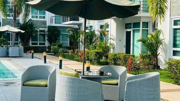 A modern outdoor seating area with wicker furniture and umbrellas, surrounded by lush greenery and a pool. - Cozy 1 bedroom condo inside Subic Bay Freeport Zone with complete amenities. (Subic Bay Freeport Zone)