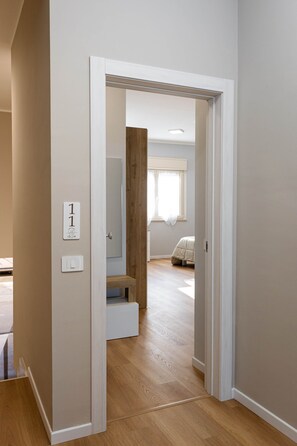 A hallway leading to a bedroom with a wooden floor, a bed, and a window with curtains. - Studio Apartment (Margherita di Savoia)