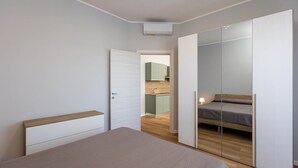 A bedroom with a bed, a wardrobe, and a small kitchenette in the background. - Sea View Apartment (Margherita di Savoia)