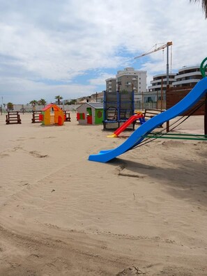 A sandy beach with playground equipment, including a blue slide and small colorful playhouses. - Two-room apartment with sea view (Margherita di Savoia)