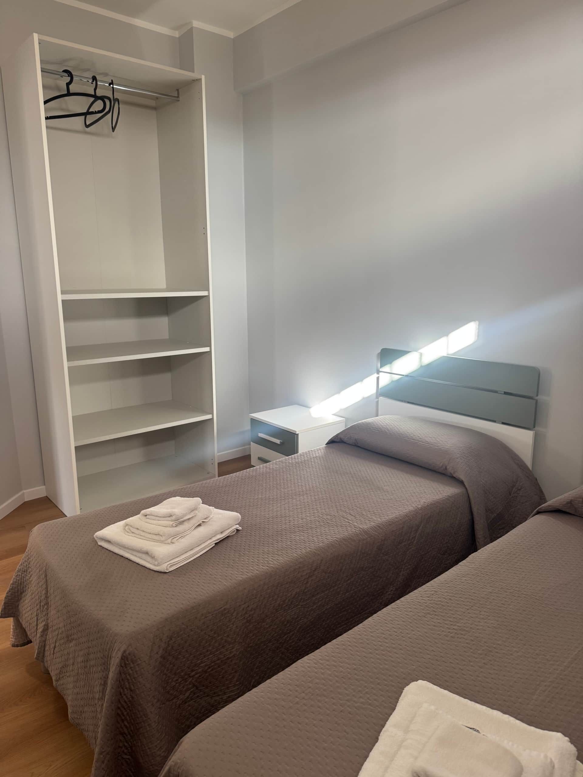 Quarto com duas camas, guarda-roupa, mesa de cabeceira e criado-mudo.