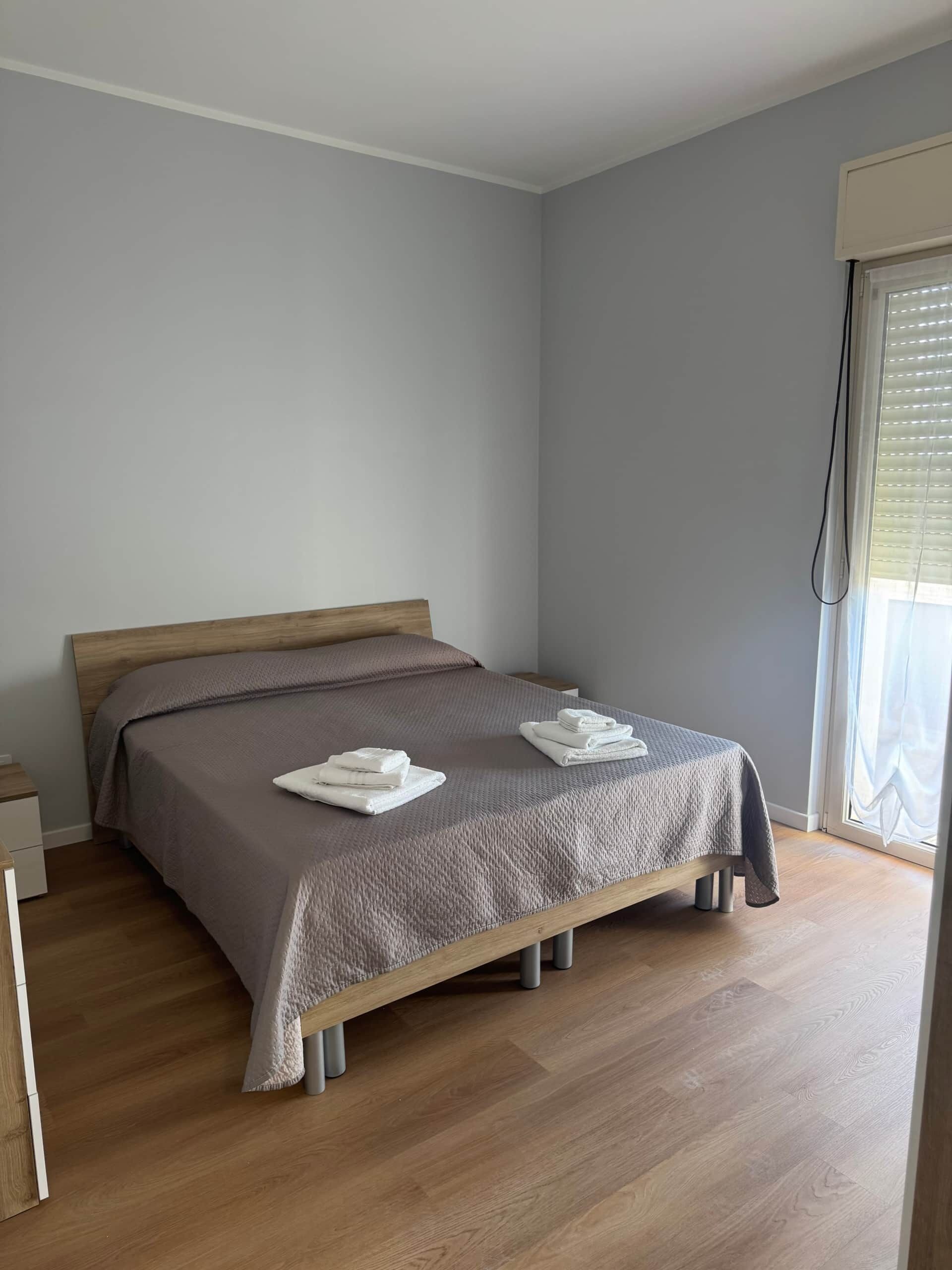 A bedroom with a bed, wooden headboard, grey walls, and a window with blinds.