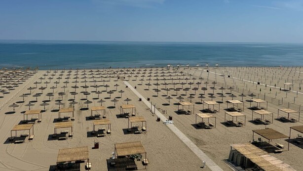 Una spiaggia con file di ombrelloni e lettini, cielo sereno e l'oceano sullo sfondo.