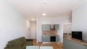 Un espace de vie moderne comprenant un canapé, deux fauteuils, une table en bois, un coin cuisine avec des placards, un téléviseur et un lave-vaisselle.