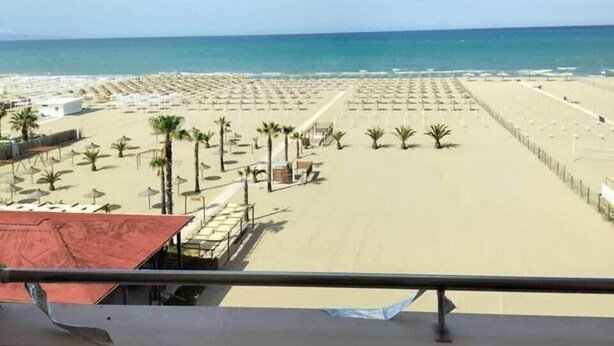 Une plage bordée de rangées de parasols et de chaises longues, un ciel dégagé et l’océan en toile de fond.