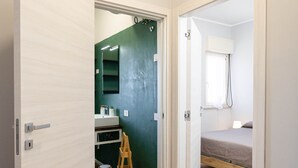 A bedroom with a wooden floor, a bed, a window, and a bathroom visible through an open door. - Sea View Apartment (Margherita di Savoia)