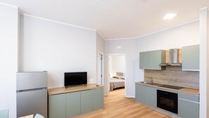 A modern kitchen with a refrigerator, stove, and sink. There is a television on the counter and a bed in the background. - Sea View Apartment (Margherita di Savoia)