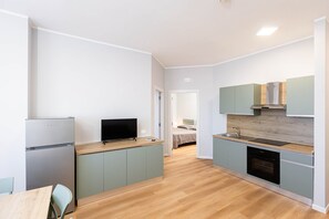 A modern kitchen with a refrigerator, stove, and sink. There is a television on the counter and a bed in the background. - Sea View Apartment (Margherita di Savoia)