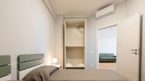 A bedroom with a bed, a nightstand, a wardrobe, and an open door to a living area. - Sea View Apartment (Margherita di Savoia)
