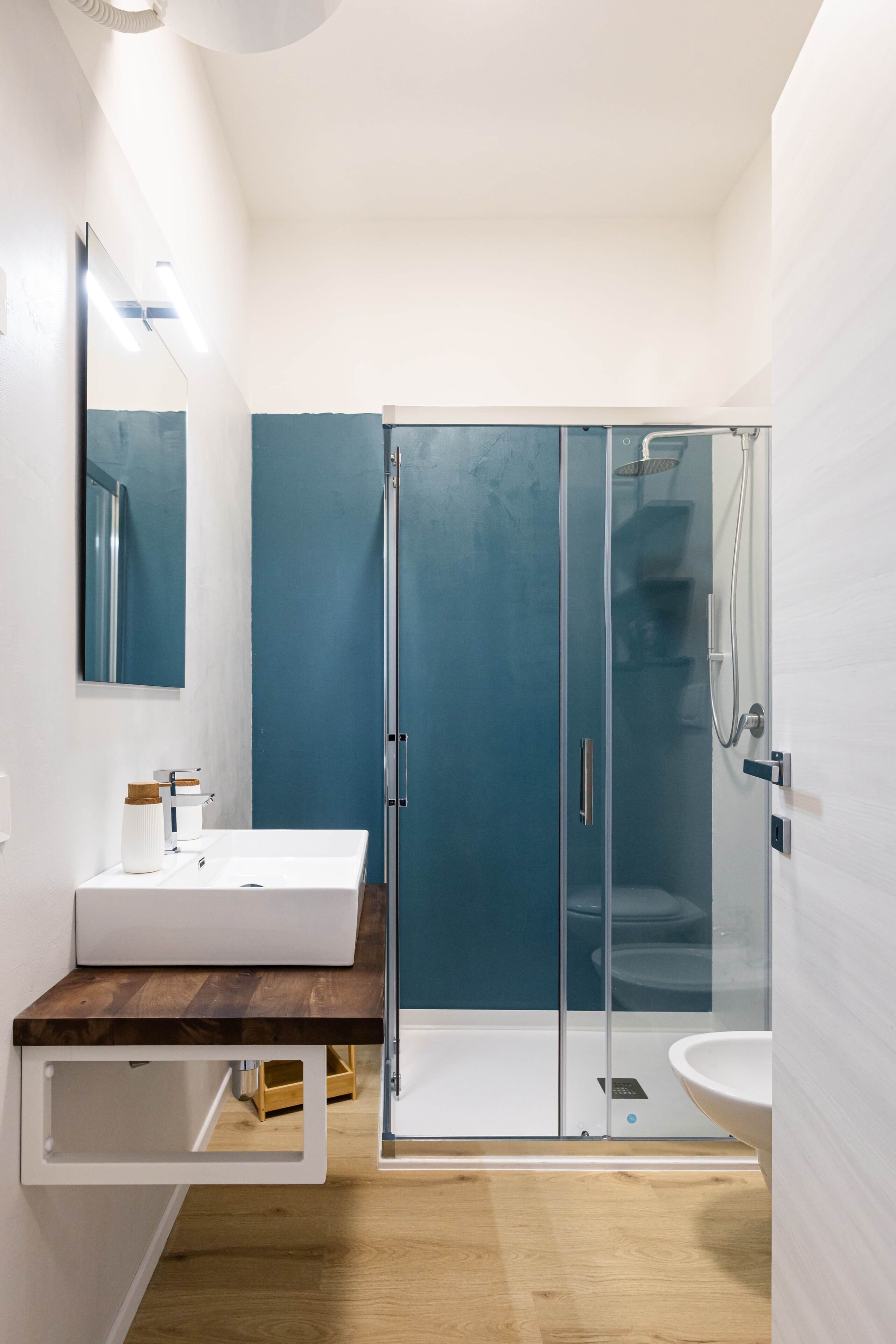 Une salle de bain moderne avec un lavabo blanc, un miroir, une cabine de douche en verre et un meuble-lavabo en bois.