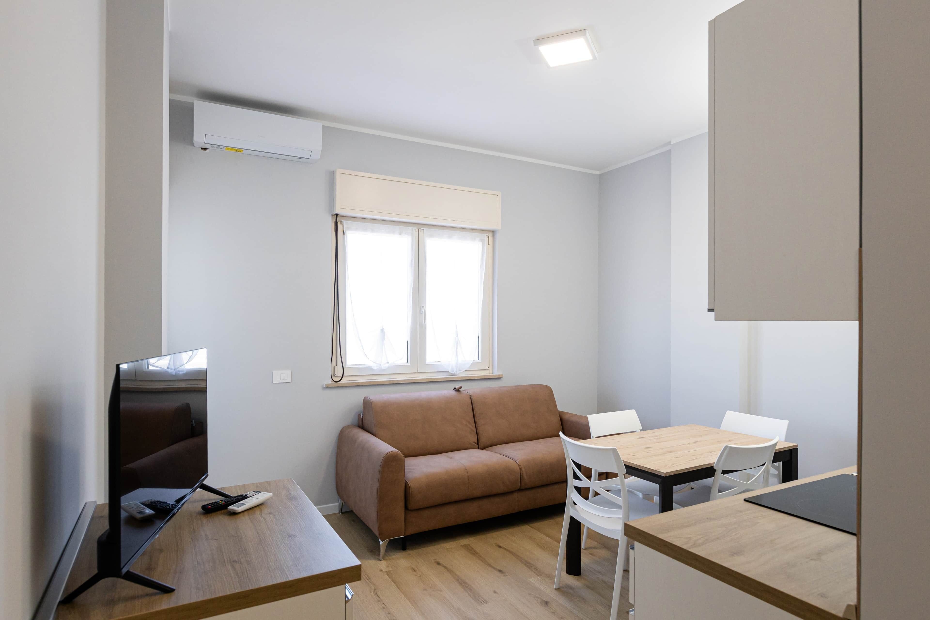 A small, modern room with a brown sofa, a wooden dining table, and a TV.
