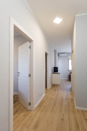 Un corridoio con pavimento in legno, pareti bianche e una luce a soffitto.
